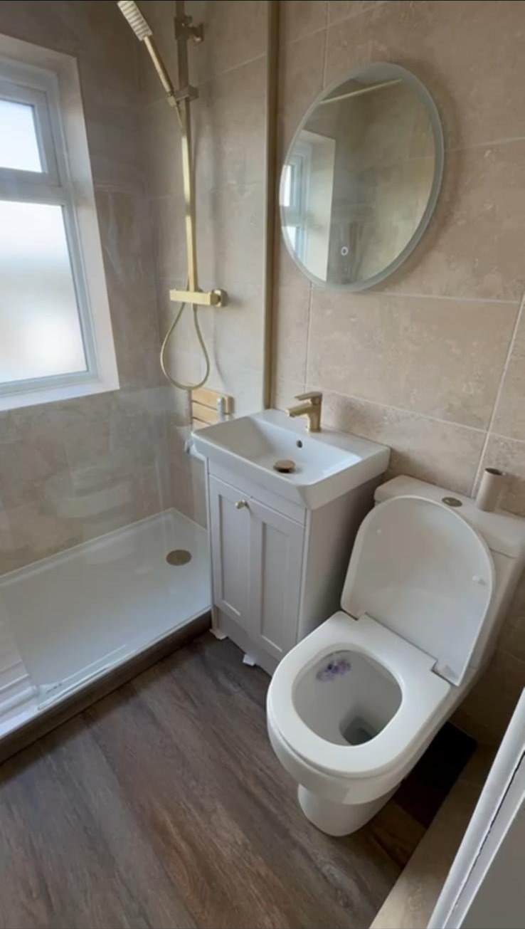 Shower tray, grey vanity unit and toilet with brushed gold shower fittings