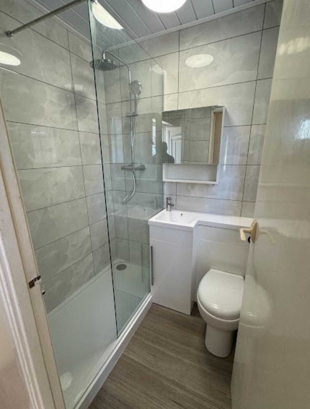 Corner shower enclosure with white tiling, vanity unit and toilet