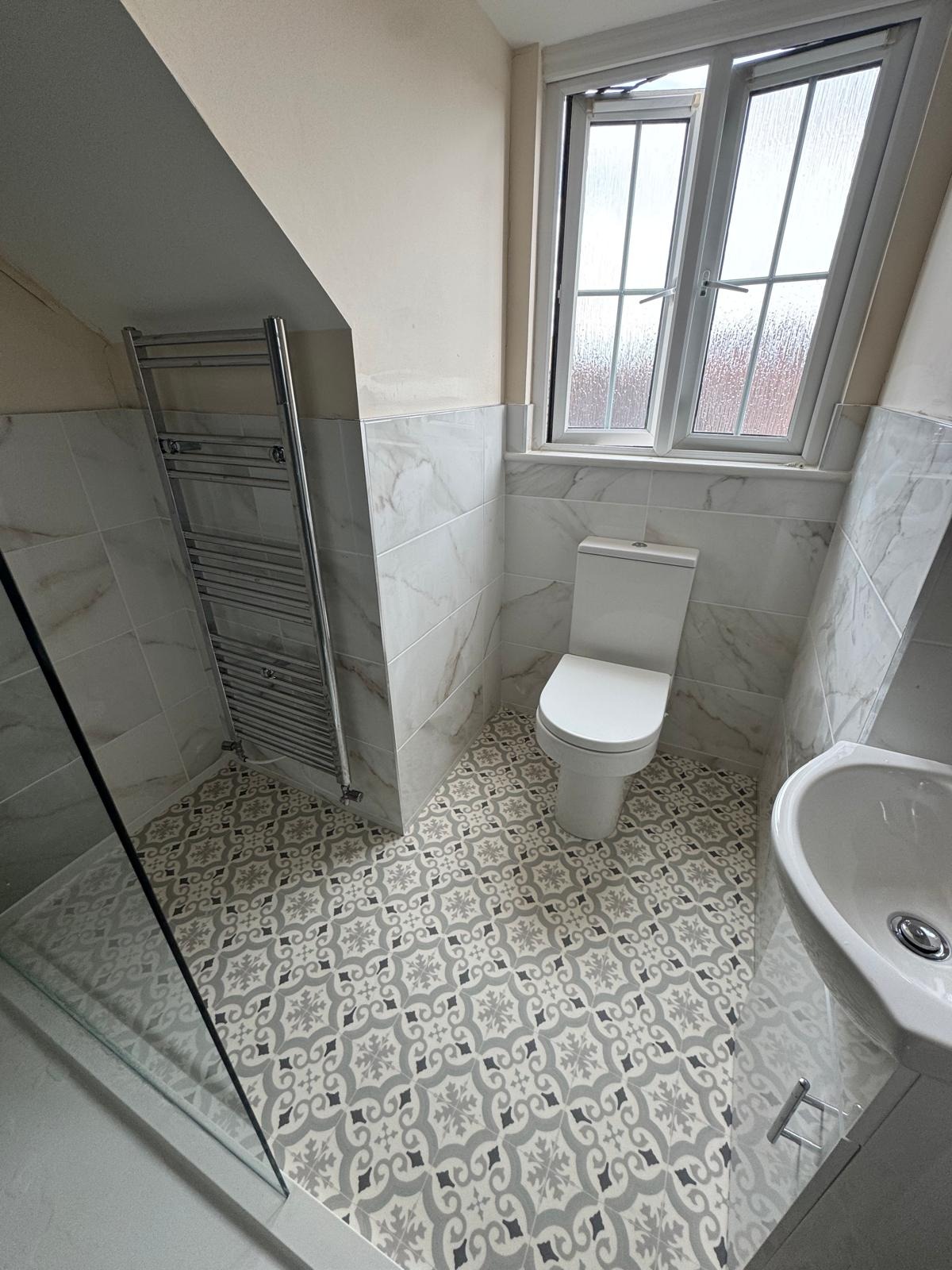 Cloakroom with towel rail, toilet and patterned floor tiles under a sloped ceiling