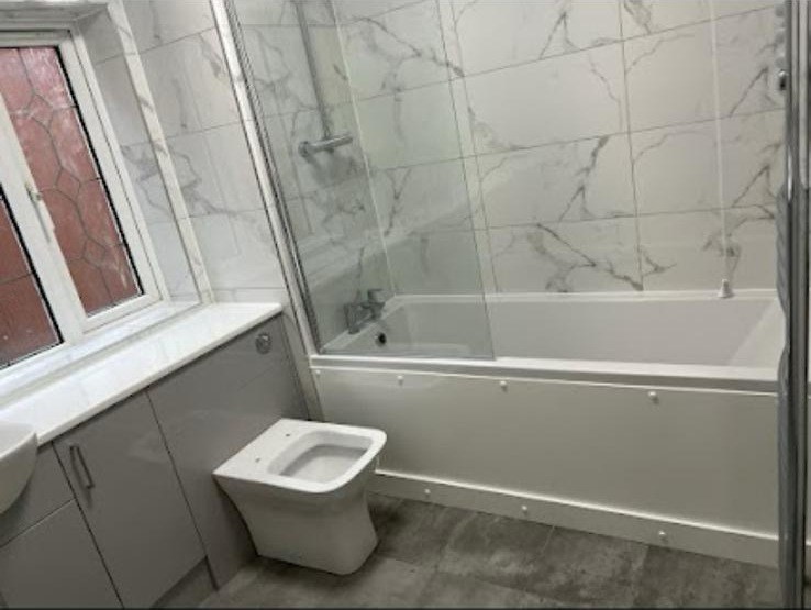 White bath fitted alongside a grey vanity unit in a refitted bathroom
