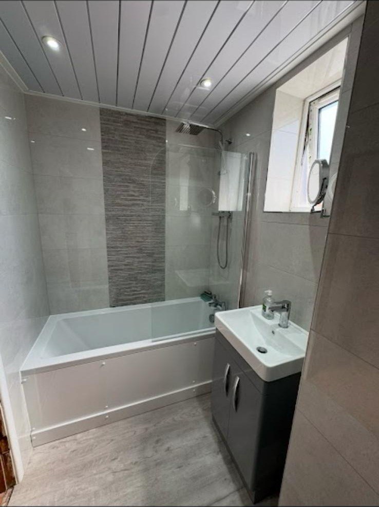 Bath and shower combination with grey vanity unit and decorative tile border