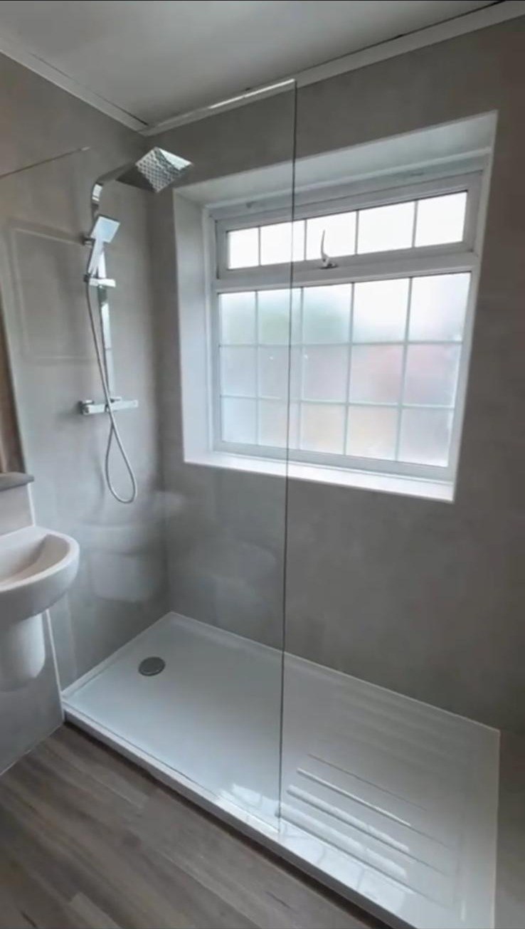 Walk-in shower with large grey wall tiles and rainfall shower head beside a window