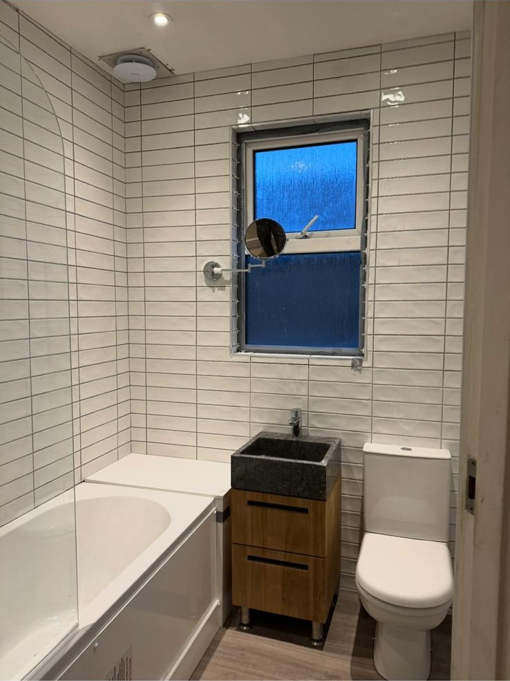 White metro tiling with contrast grout around a bath, timber vanity and toilet