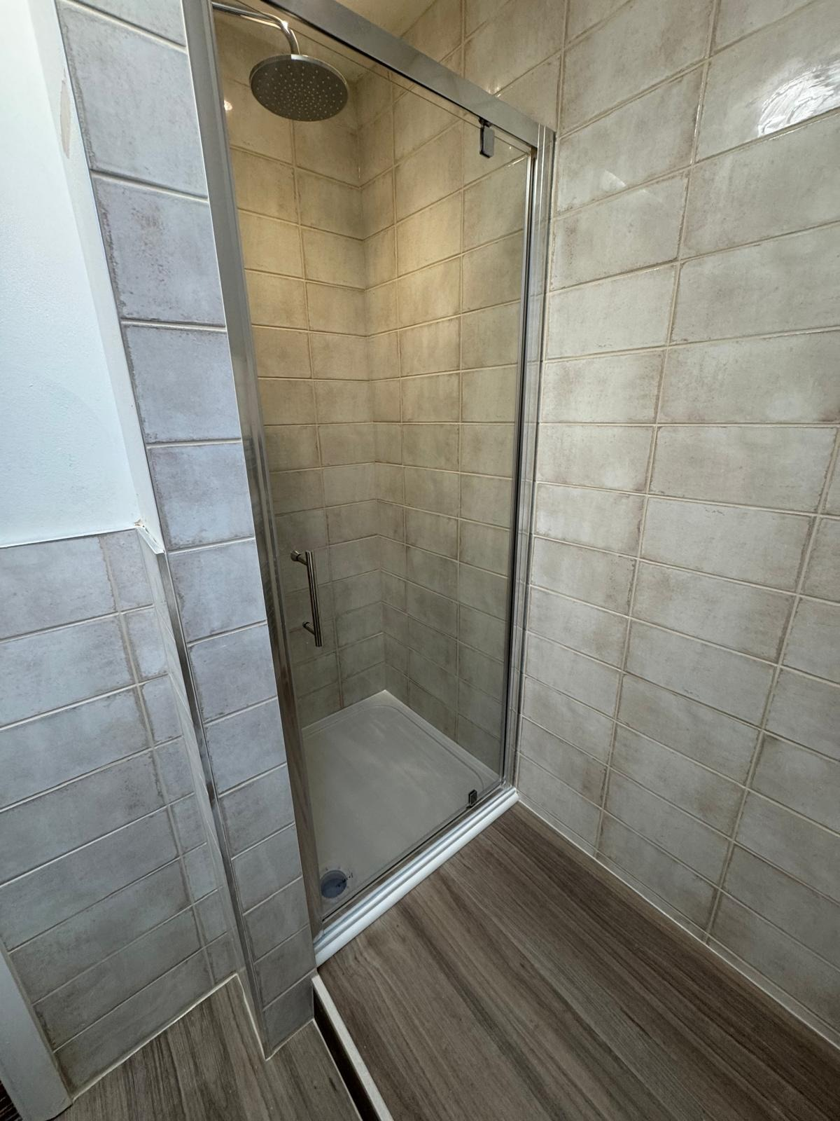 Stone-effect wall tiling around a shower enclosure with wood-effect flooring in a tiled bathroom