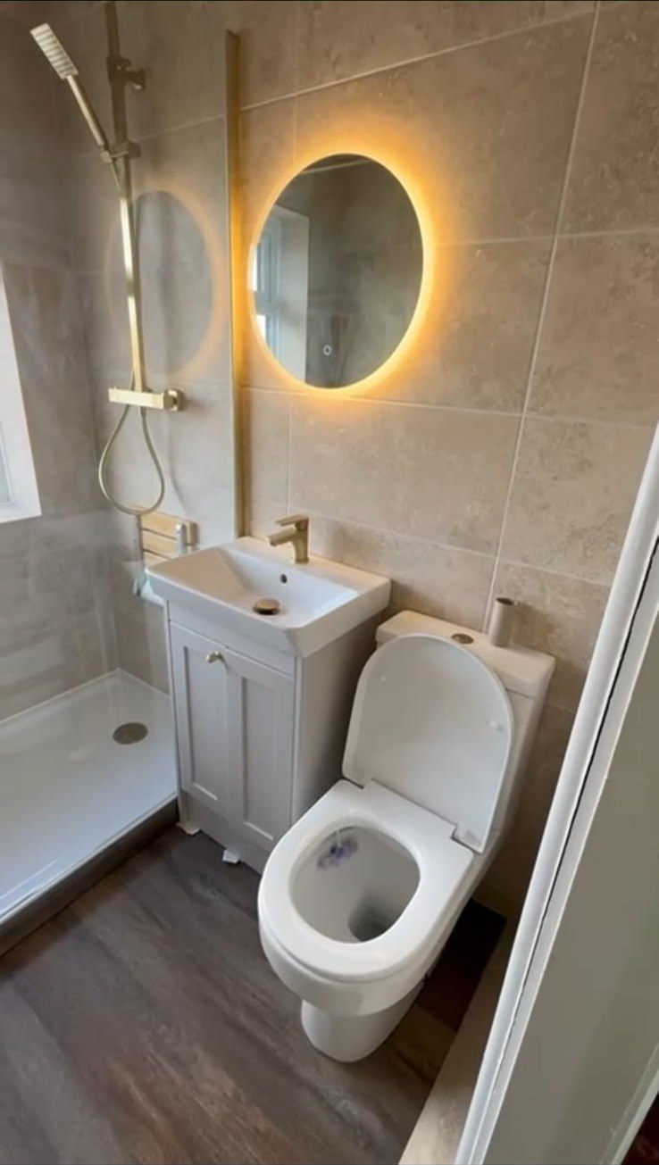En-suite with beige tiling, brushed gold shower fittings and backlit round mirror