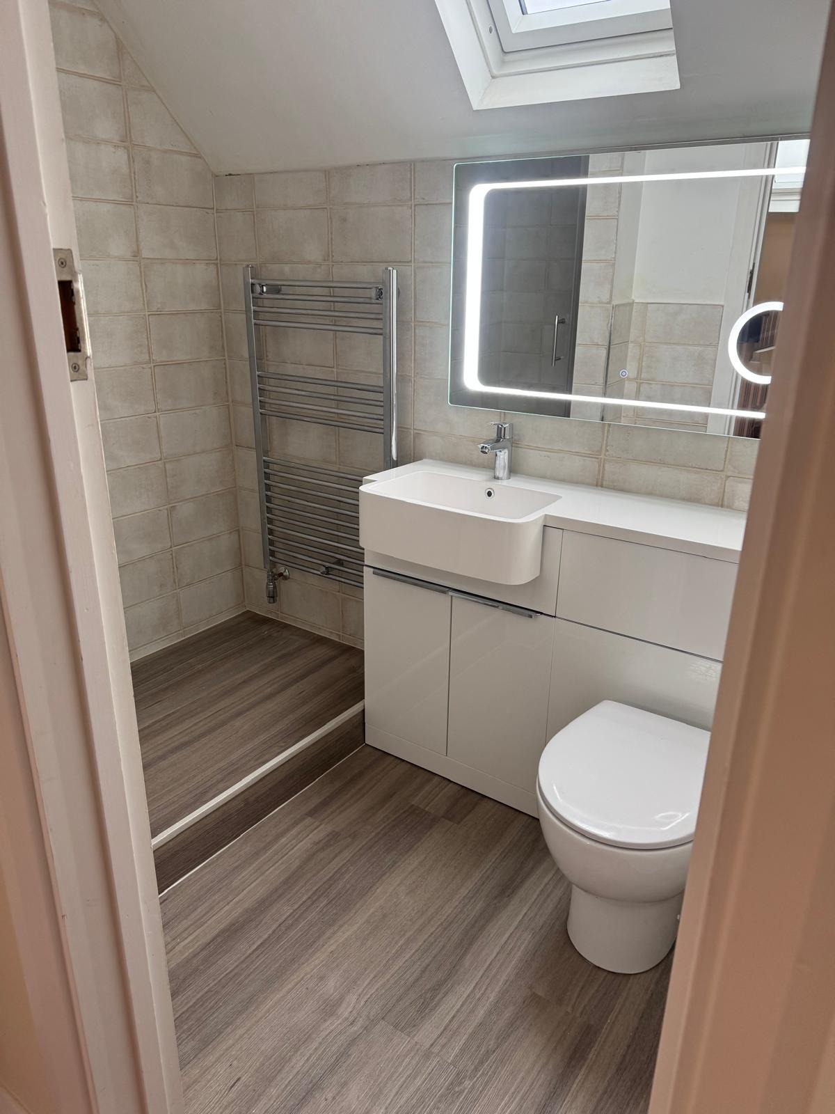 Loft bathroom with combined vanity and toilet unit, LED mirror and chrome towel rail