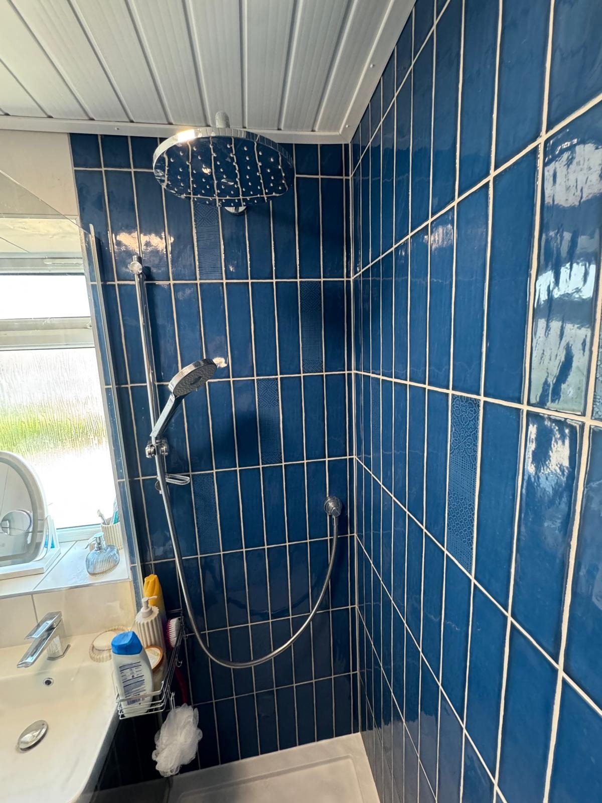 Vertically stacked blue gloss wall tiling around a shower with rainfall head