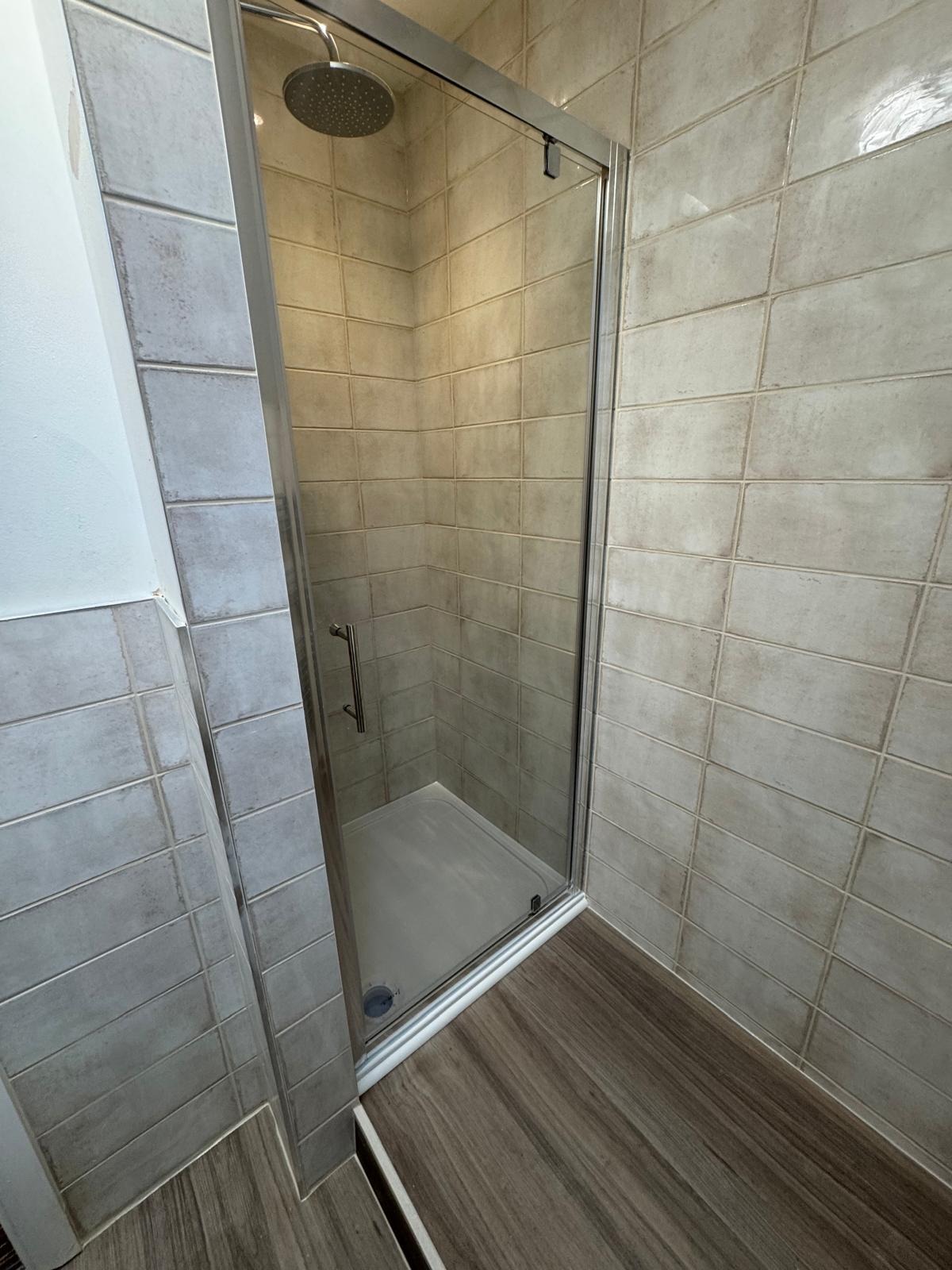 Walk-in shower with textured grey wall tiles and wood-effect flooring
