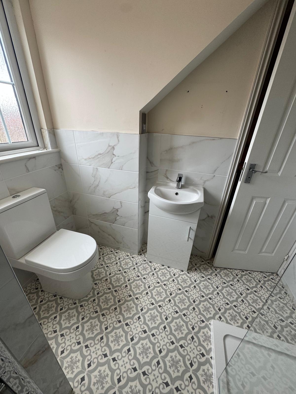 Cloakroom refit with patterned floor and marble-effect wall tiles under a sloped ceiling