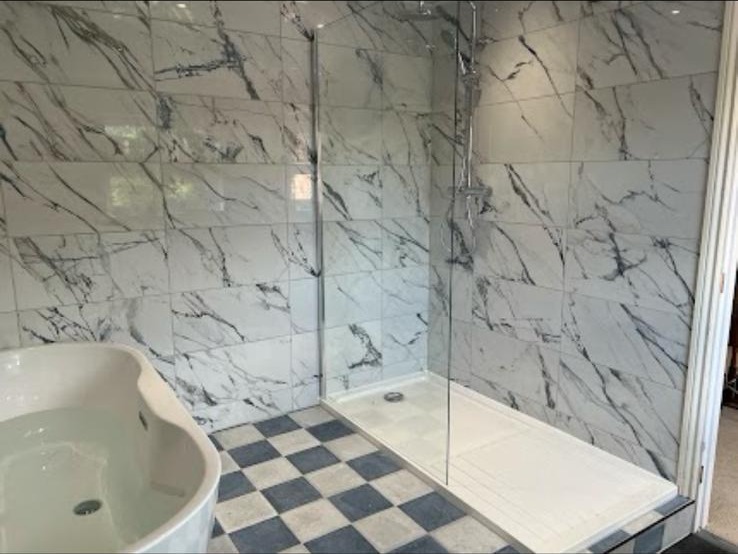 Walk-in shower area with marble-effect tiling and chequerboard floor beside a bath