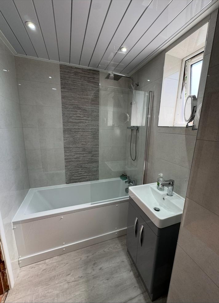 Shower over bath with glass screen, grey wall tiling and vanity unit
