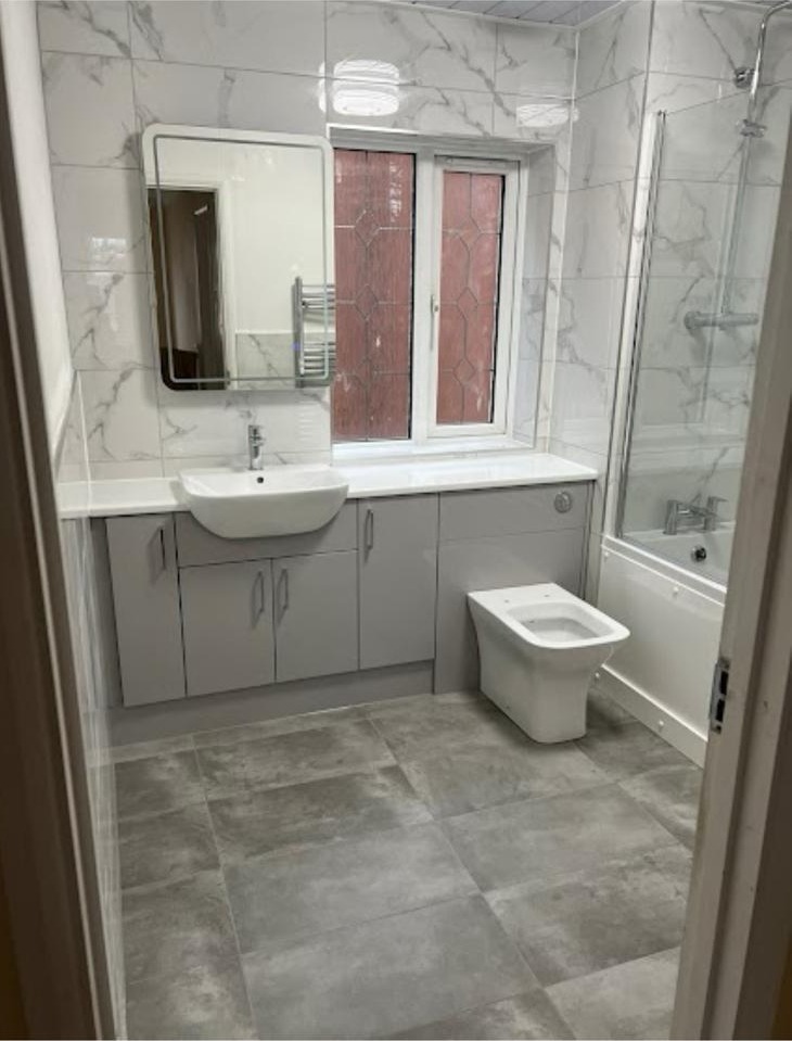 Grey vanity unit with white basin and toilet in a fully tiled bathroom