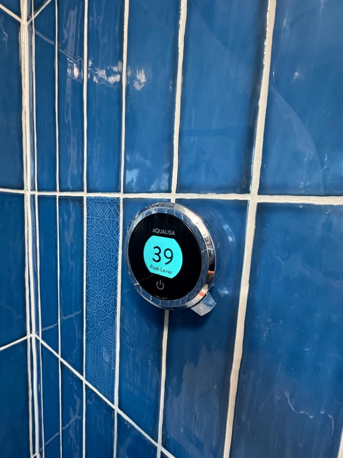Wired digital shower control set to 39 degrees on blue gloss tiling
