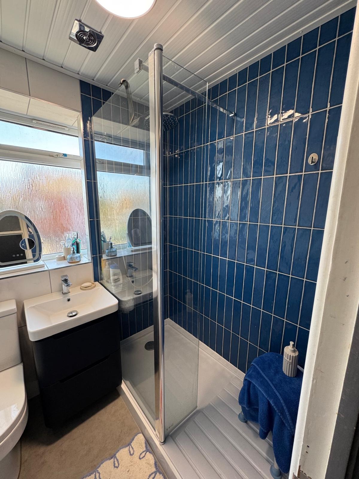 Blue-tiled shower with digital control beside a black vanity unit