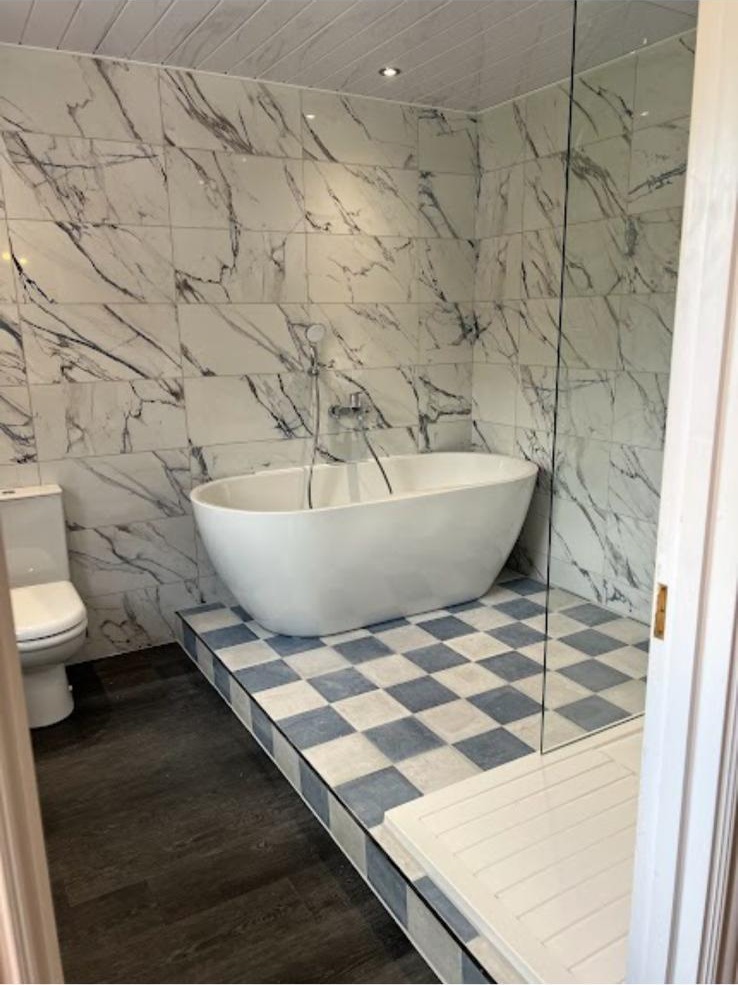 Freestanding bath on a chequerboard tiled platform with marble-effect walls